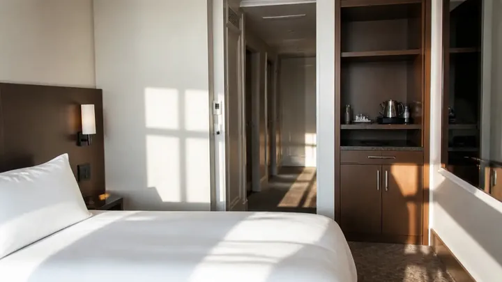 Empty hotel room showing a bed, doorway, and wet bar cabinet