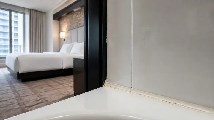 Bathtub corner with a caulk seam and a bed through the doorway