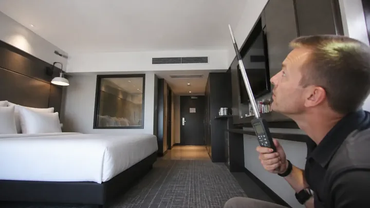 Man holding a measuring device near a hotel room ceiling vent