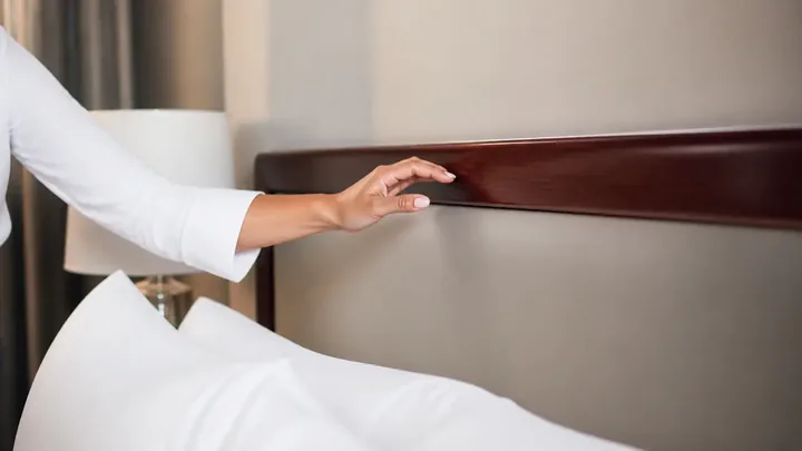Hand touching a dark wood headboard rail above white bedding