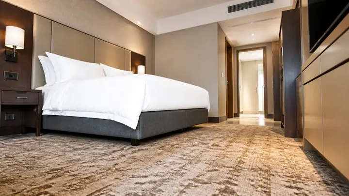 A furnished guestroom with a made bed, wall-mounted reading light and television