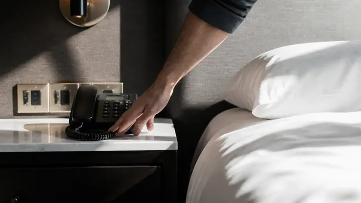 Hand reaching for a phone and light switches on a nightstand