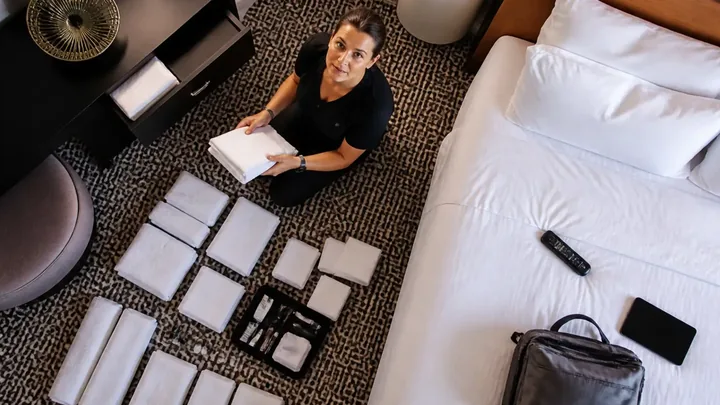 Overhead view of a woman sorting hotel amenities beside the bed